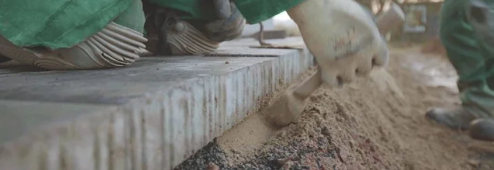 Person ebnet Sand vor Randsteinen mit Hilfe eines Hammers